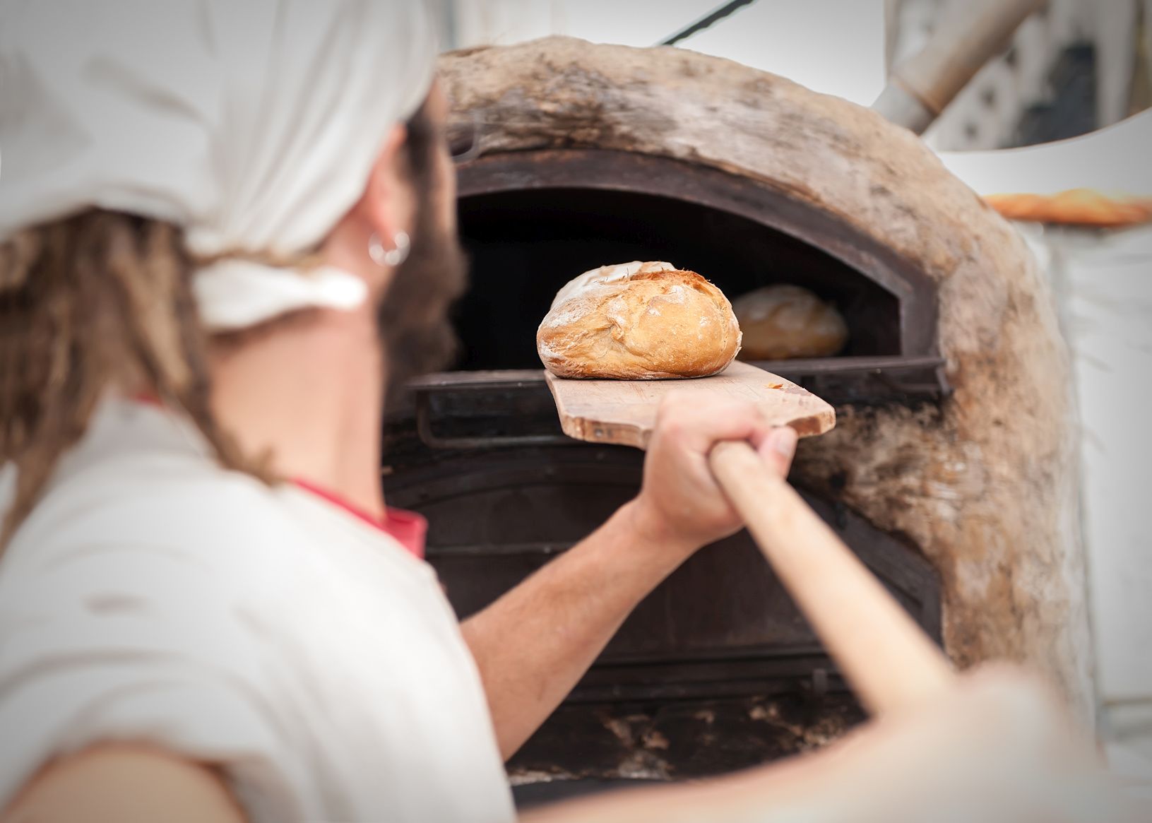 Bäcker schiebt einen Brotlaib in einen Steinofen
